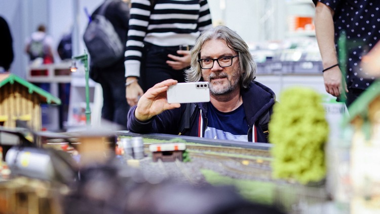 Hobbymesse Leipzig: Ein Mann fotografiert mit seinem Handy eine Modelleisenbahnanlage