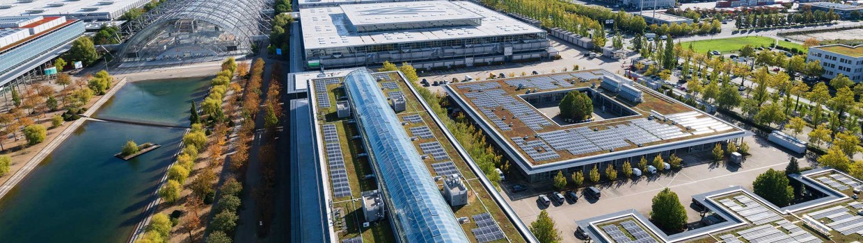 Blick auf den Messe-See mit Glashalle und das begrünte Dach vom Verwaltungsgebäude mit Photovoltaik-Anlage